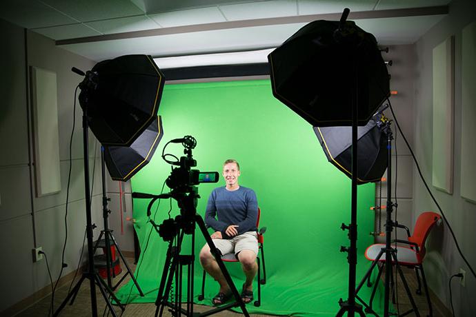 student sits in front of green screen in studio